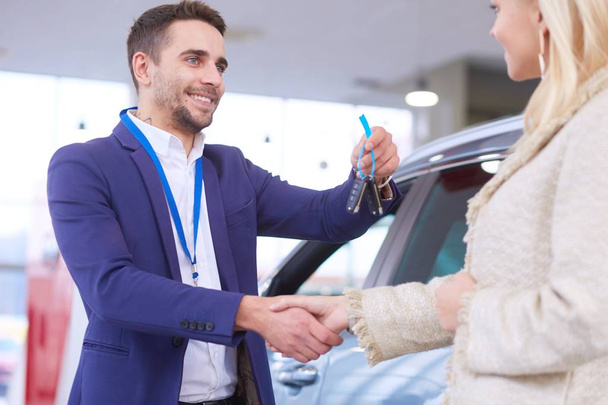 Image of car dealer handshaking with happy female in automobile center - Zdjęcie, obraz