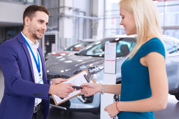 Car salesman sells a car to happy customer in car dealership and hands over the keys - Foto, imagen
