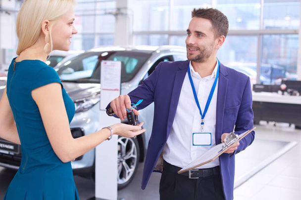 Car salesman sells a car to happy customer in car dealership and hands over the keys - Foto, Bild