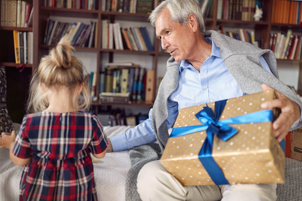 Giving Christmas gift on celebration time- grandfather with gift for his little granddaughter - 写真・画像
