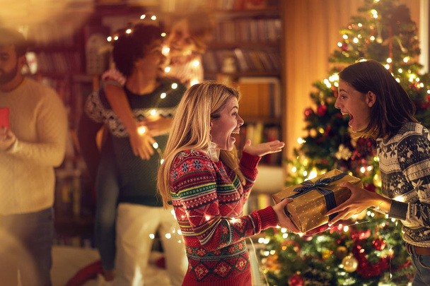 Happy girl surprising her friend girl with a present at Christmas - Fotografie, Obrázek