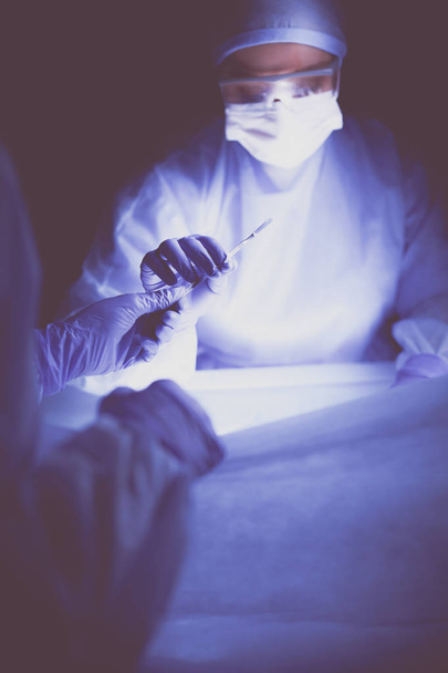 Doctor performing surgery in a dark background. - Valokuva, kuva