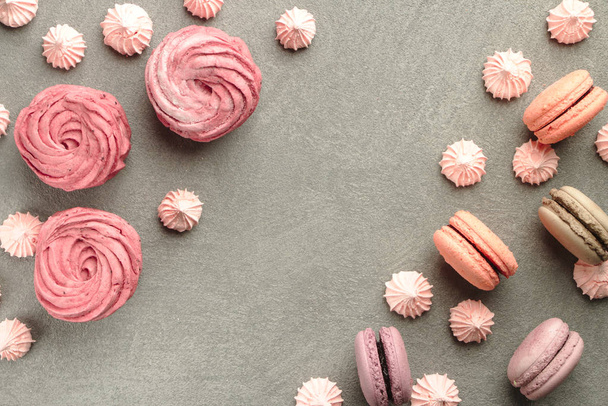 Sweets on grey concrete background: macarons, marshmallow and meringue of different pastel colours. Frame and a pattern of colorful french cookies, marshmallow and meringue. Valentine's Day background - Photo, image