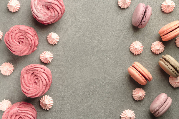 Sweets on grey concrete background: macarons, marshmallow and meringue of different pastel colours. Frame and a pattern of colorful french cookies, marshmallow and meringue. Valentine's Day background - Photo, image
