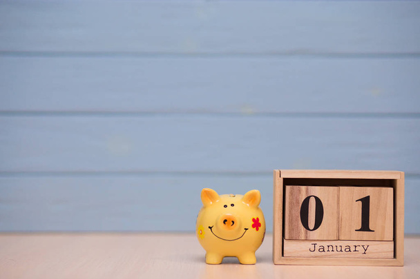 Календарь даты начала финансового года, 1 января с копилкой свиньи на синем фоне. Зимнее время. Новогодняя концепция
 - Фото, изображение