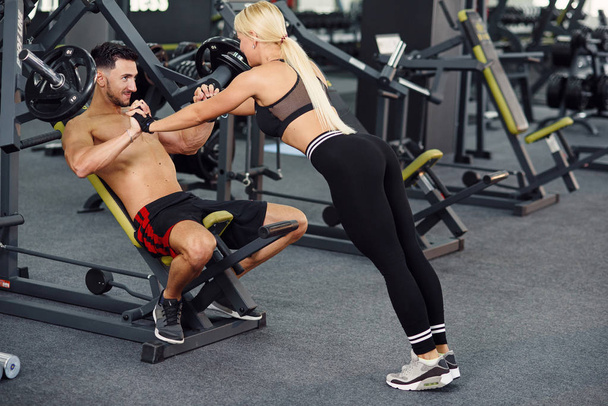 Muscular healthy guy and his sporty girlfriend training together in the gym. Lovely couple training together at the gym. Fitness and bodybuilding concept. - Foto, imagen