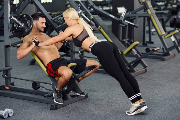 Muscular healthy guy and his sporty girlfriend training together in the gym. Lovely couple training together at the gym. Fitness and bodybuilding concept. - 写真・画像