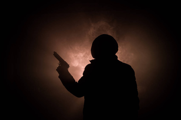 Silhouette d'homme avec pistolet prêt à attaquer sur fond brumeux foncé ou dangereux bandit tenant pistolet à la main. Tir terroriste avec décor de thème d'arme
 - Photo, image