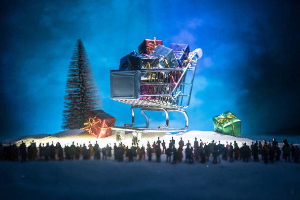 Uusi vuosi tai joululoma ostoksia käsite. Kaupan tarjouksia. Siluetti suuri joukko ihmisiä katsomassa iso ostoskärry lahjoja. Ihmiset lumessa valmiina ostoksille. Valikoiva painopiste
 - Valokuva, kuva