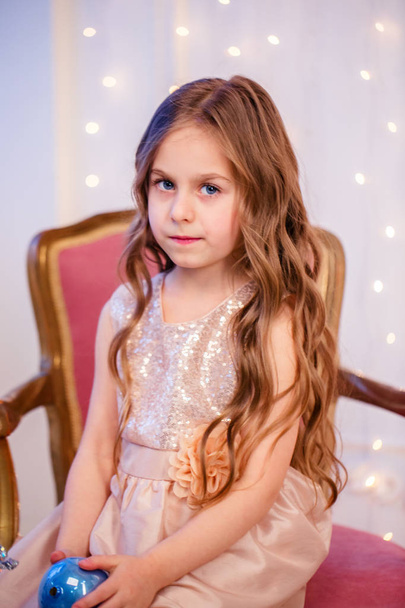 Portrait of a little girl with curly hair on Christmas Eve, the New Year will bring gifts. Cheerful emotions in anticipation of a surprise. - Zdjęcie, obraz