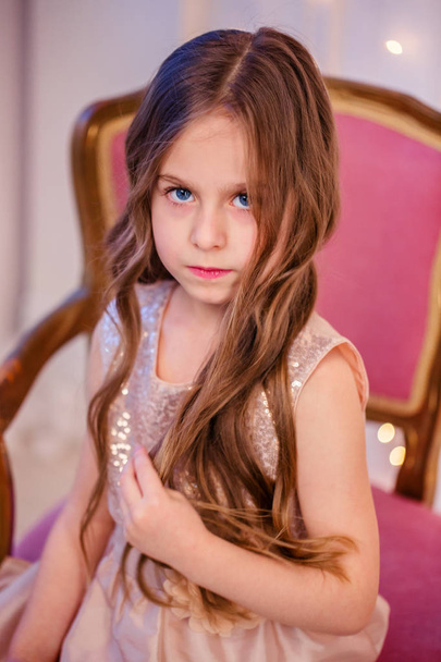 Portrait of a little girl with curly hair on Christmas Eve, the New Year will bring gifts. Cheerful emotions in anticipation of a surprise. - Фото, зображення