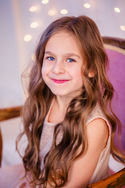 Portrait of a little girl with curly hair on Christmas Eve, the New Year will bring gifts. Cheerful emotions in anticipation of a surprise. - Foto, Bild