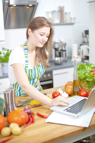 Kochende Frau schaut beim Zubereiten von Essen in der Küche auf den Computer - Foto, Bild