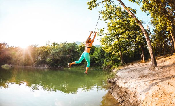 Skočit do vody. Žena odpočívá na jezeře. Swing lano a klacek. Aktivní odpočinek v přírodě. Letní zábavy. Žena na koni houpačka. Objektiv s rybím okem. - Fotografie, Obrázek