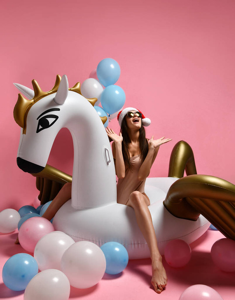 Young girl with pastel air balloons on birthday holiday party having fun celebrating with unicorn pegasus float in Santa hat  - Фото, зображення