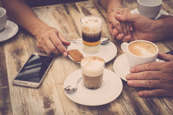 Close up of aged hands with coffee at wooden table  - Photo, Image
