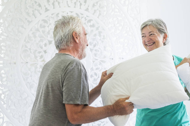 遊び心のある大人の年配の男性と女性の白人カップルのため自宅枕戦争  - 写真・画像
