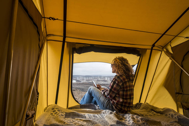 Free alternative holiday woman inside a tent looking at the panorama outside and use technology internet connected mobile phone to stay connected with the rest of the civilized world. - Foto, Imagen