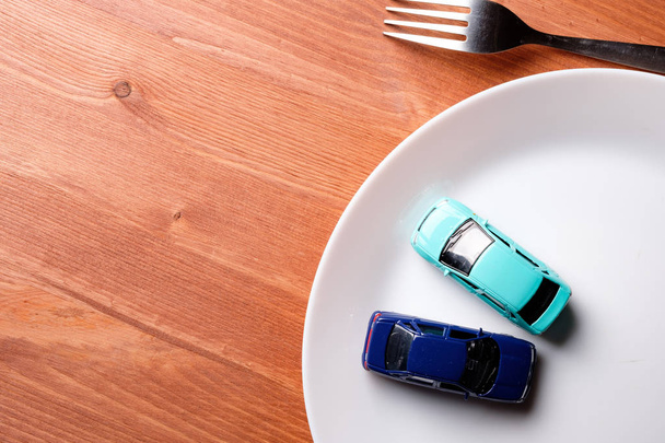 twee speelgoedmodellen van de auto, en wel in een witte plaat samen met een vork op een houten tafel - Foto, afbeelding