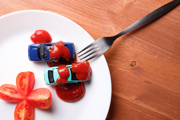 verdeeld in vier delen tomaat ernaast zijn twee auto's bedekt met een laagje ketchup, het is allemaal in een witte plaat op een houten tafel - Foto, afbeelding