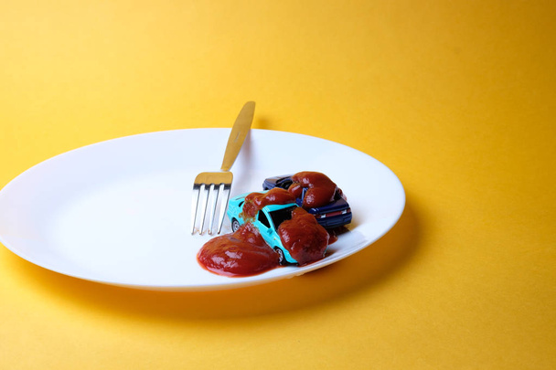 side view of the plate with ketchup and toy cars and a stainless steel fork, background yellow - Фото, зображення