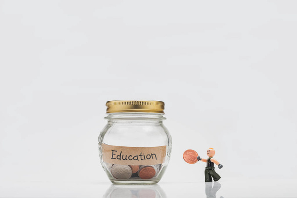 Studio shooting of a miniature figure of a man from Lego carries money in the piggy bank for education. Photo isolated on white background. - Photo, Image