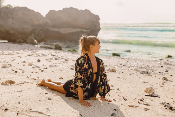 Mujer atractiva practica yoga en la playa con puesta de sol o salida del sol
. - Foto, imagen