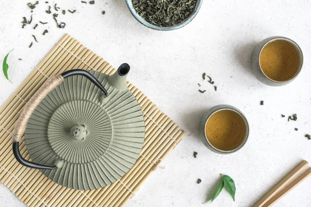Asian Tea Set -  iron teapot and ceramic teacups with green tea. Traditional tea composition on white background with bamboo mat, top view. - Fotó, kép