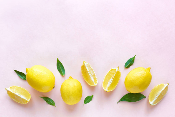 Lemons with green leaves on pink pastel background, top view, copy space. Organic fresh citrus fruits lemons, minimal conceptual flat lay. - Foto, immagini