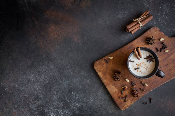 Traditional indian masala chai tea in ceramic cup with ingredients. Spicy black tea with milk (Masala) on rustic dark background, copy space. - Foto, imagen