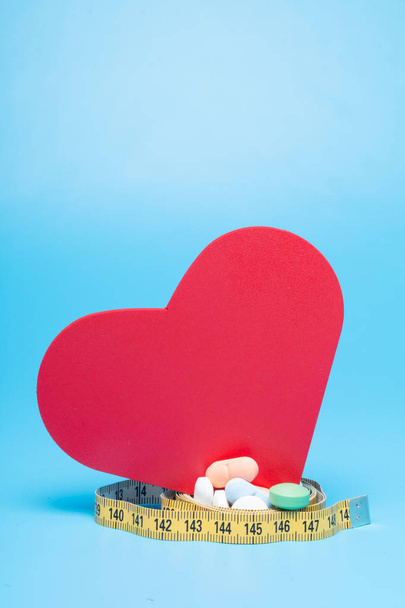 Tape measure, pills and a red heart on a blue background - Фото, зображення