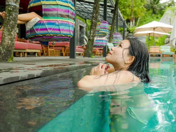 lifestyle portrait of young attractive and beautiful Asian Korean woman relaxing happy at tropical beach resort swimming at hotel pool enjoying Summer holidays in paradise island - Valokuva, kuva