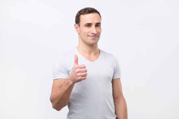 Aantrekkelijke man duim opdagen op camera met happy glimlach geïsoleerd op witte achtergrond - Foto, afbeelding
