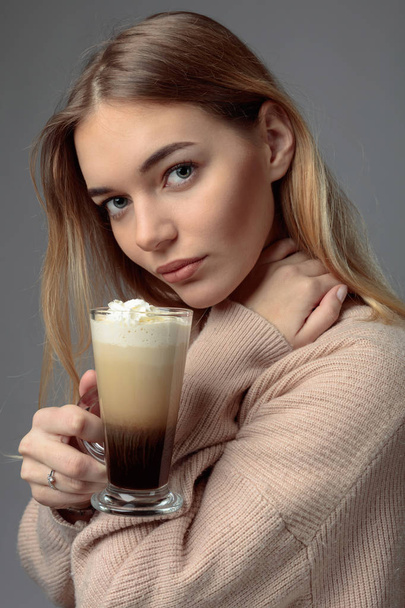 Atrakcyjna, młoda kobieta z kawa po irlandzku. Piękna Blondynka w swetrze, trzymając kubek kawy ze śmietanką. - Zdjęcie, obraz