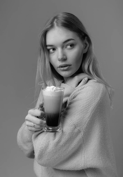 Attractive young woman with Irish coffee. Beautiful blonde in a sweater holding a mug of coffee with cream. - Fotó, kép