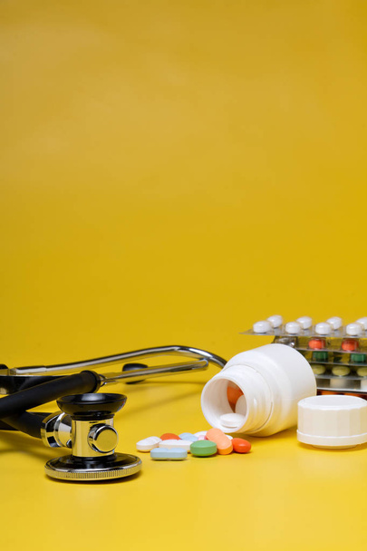 Tabletták és sztetoszkóp, sárga háttérrel - Fotó, kép