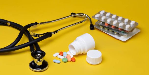 Pillen en stethoscoop op een gele achtergrond - Foto, afbeelding