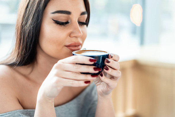 Close up of young beautiful woman holding cup of coffee and enjoying its aroma. - Φωτογραφία, εικόνα