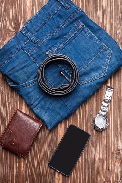 Vaqueros, cinturón y billetera, accesorios para hombre sobre mesa de madera marrón
 - Foto, Imagen