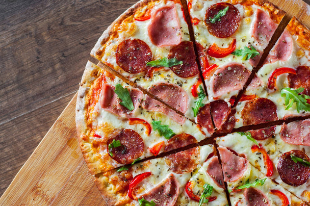 Pizza with Mozzarella cheese, ham, tomato sauce, salami, pepper, Spices and Fresh arugula. Italian pizza on wooden table background - Foto, afbeelding