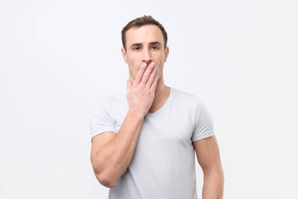 Σοκαρισμένος νεαρός ιταλική σε λευκό t-shirt που καλύπτουν το στόμα με τα χέρια και κοιτάζοντας κάμερα - Φωτογραφία, εικόνα