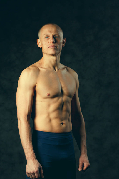 Muscular model sports young man on dark background. Fashion portrait of strong brutal guy with a modern trendy hairstyle. Sexy torso. Male flexing his muscles. Sport workout bodybuilding concep. Toned - Zdjęcie, obraz