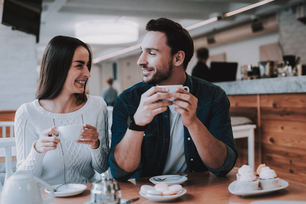 Couple Resting in Cafe. Couple is Beautiful Young Man and Woman. Couple is Drinking Tea. People is Looking on Each Other. Persons is Sitting at Table. People is Happy and Smiling. Daytime. - 写真・画像