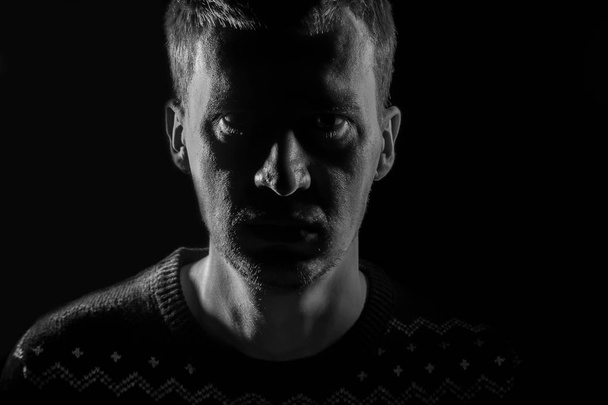 Close-up van een mysterieuze zwart-wit portret van een volwassen serieuze man in het donker, kijken naar de camera: rechte neus, oren, expressieve ogen en baard. Gezicht gemarkeerd in detail. - Foto, afbeelding