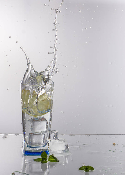A glass of lemonade on a light background with splashing water - Fotó, kép