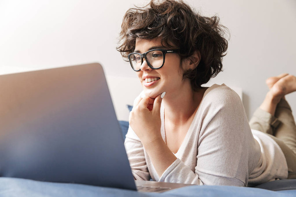 Immagine di una giovane donna felice si trova al chiuso sul letto con computer portatile
. - Foto, immagini