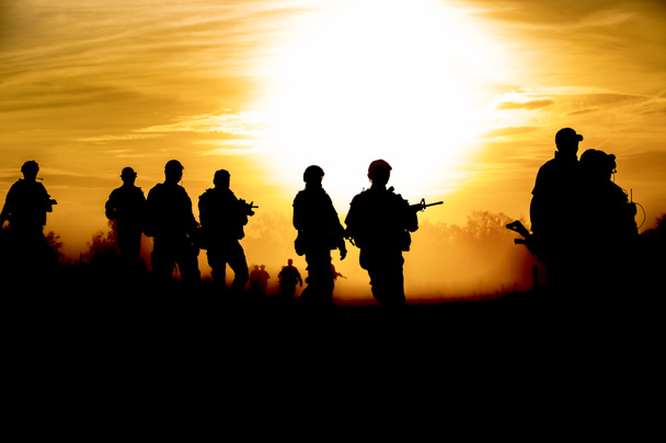 Silhouette akció katonák séta a fegyverek tartsuk lenyomva a háttérben a füst és a naplementét és a fehér egyensúly hajó hatása dark art stílusban - Fotó, kép