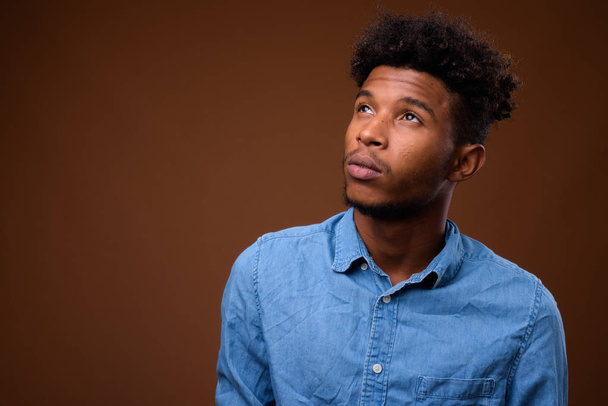 junger gutaussehender afrikanischer Mann denkt vor braunem Hintergrund - Foto, Bild