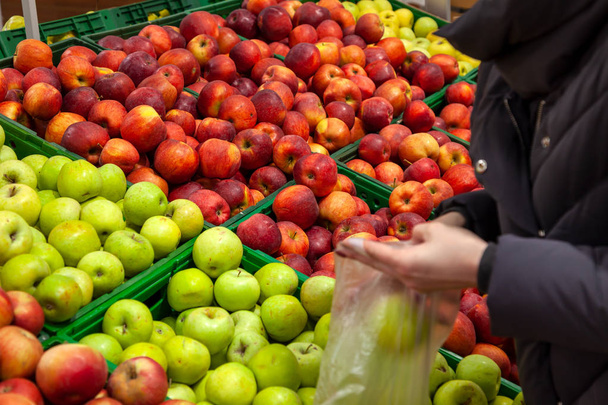 Der Käufer wählt die Äpfel an der Theke im Supermarkt und legt sie in die Verpackung, wobei er die grüne gegenüber der roten bevorzugt. eine Frau kauft Äpfel, legt grün. - Foto, Bild