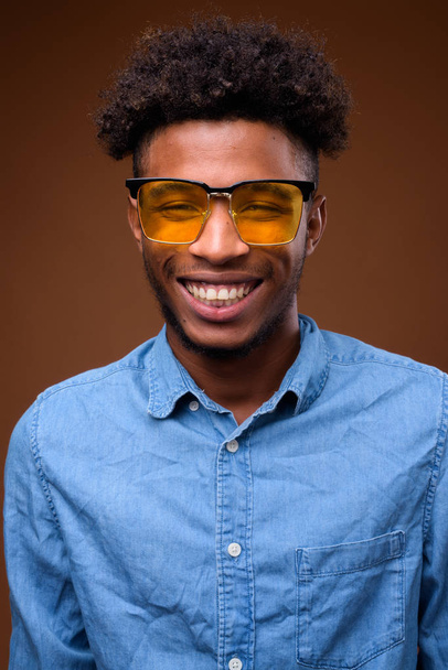 Rosto do jovem homem africano feliz sorrindo contra fundo marrom
 - Foto, Imagem